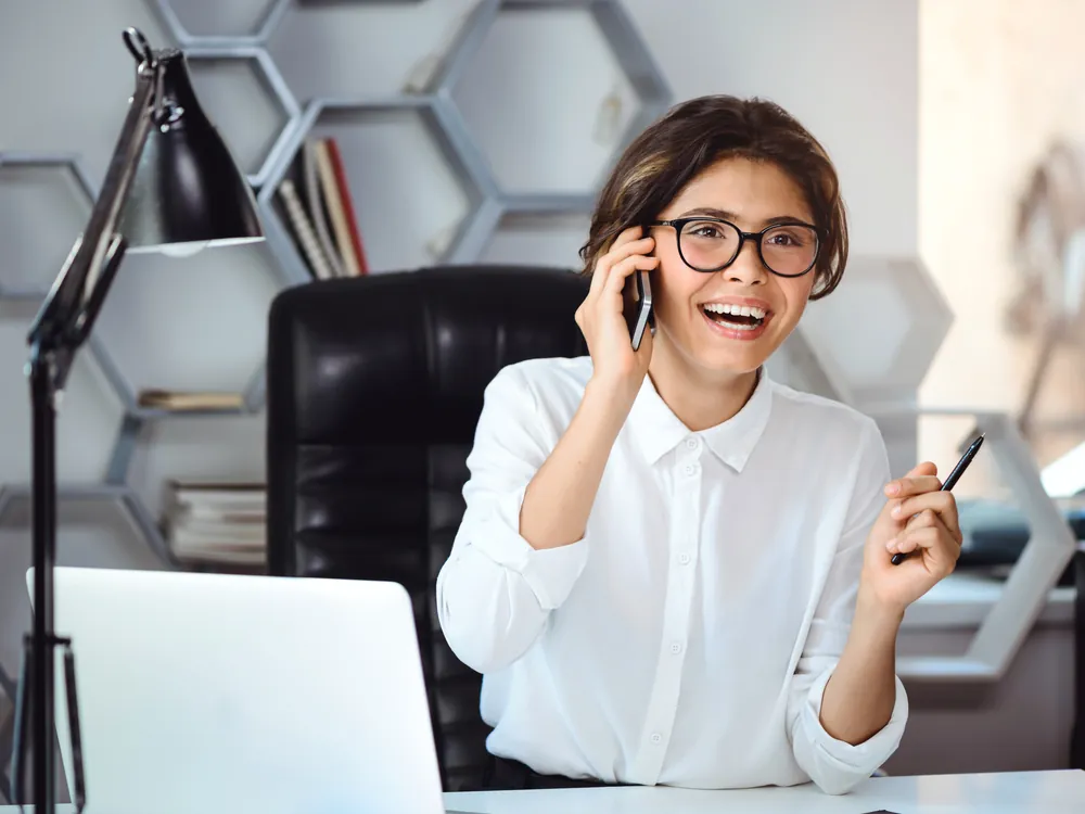 A professional taking a phone call at her desk with a laptop open — a lead reached during her working day, minutes after enquiring.