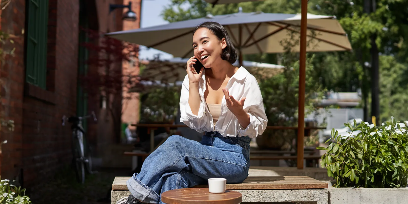 A woman smiling and gesturing mid-phone-call outside a cafe — the kind of natural back-and-forth the agent is built to hold, rather than a recorded message.